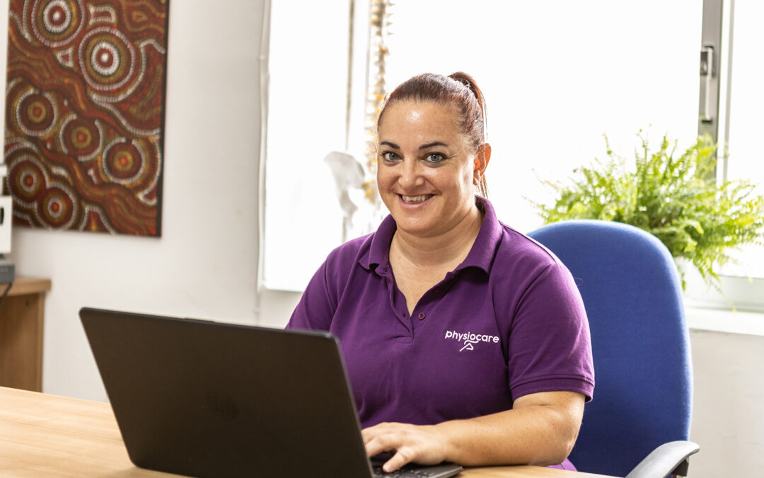 Female Physiocare staff member smiling while working on laptop in office