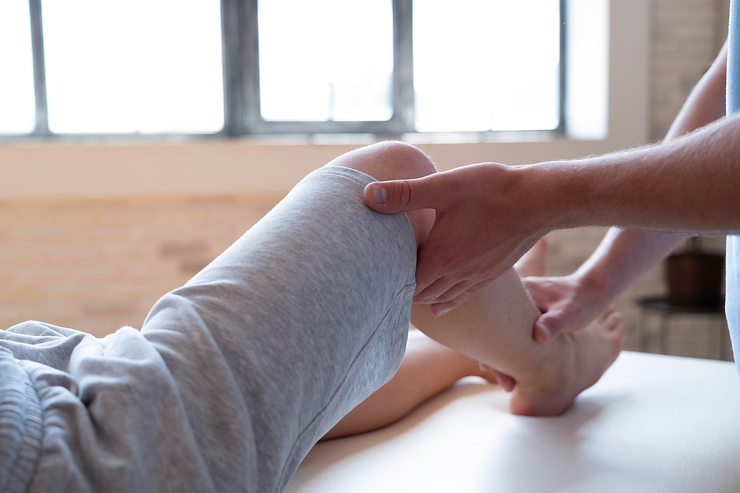 Physiotherapist performing knee assessment on a patient lying on a treatment table.