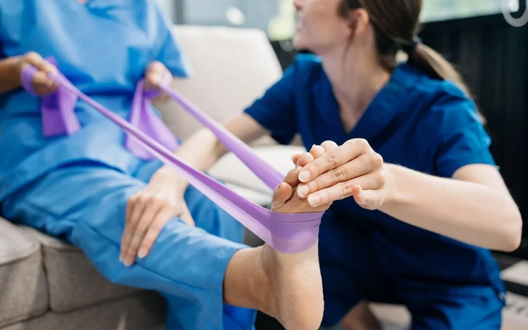 Female physiotherapist assisting an elderly woman with a foot stretch using a purple resistance band