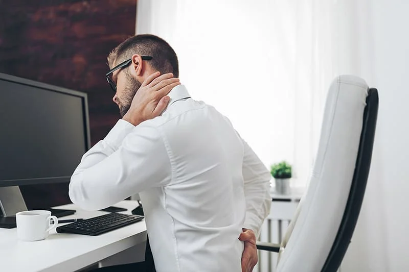 Office workers, holding his neck and back while sitting in his office, in pain.