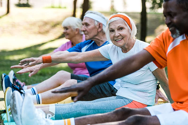 Group of elderly men and women stretching outdoors during physiotherapy exercise